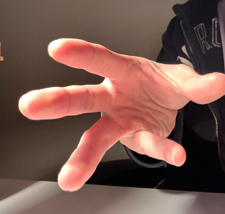 a closeup image of a person's hand reaching out towards the camera. the hand is illuminated by a light source that casts shadows across the skin. the hand appears to be grabbing or reaching for something just out of frame.