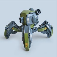 a gray and green plastic toy robot with four legs and a cannon on top. the robot is posed on a light gray background.