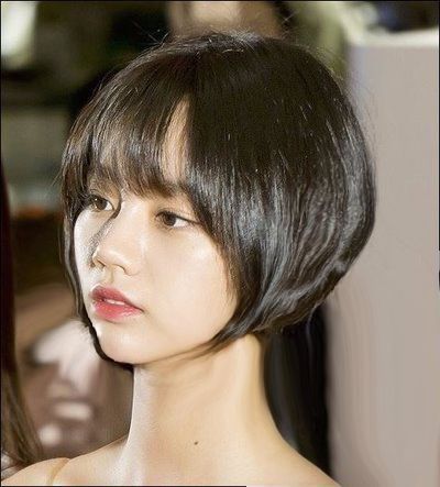 a young asian woman with dark, short bobbed hair, styled with bangs that cover her forehead, looks down with a soft, neutral expression. the focus is on her face and the elegant style of her hair. she's dressed in a simple outfit and the lighting is soft and flattering.