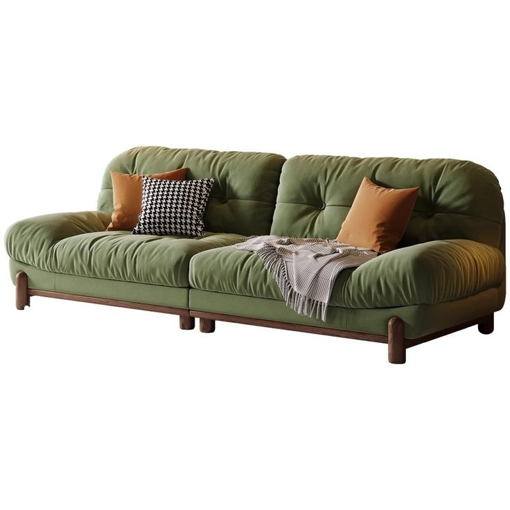 a green sofa with several cushions and a throw blanket on it. it features wooden legs and is set against a white backdrop.