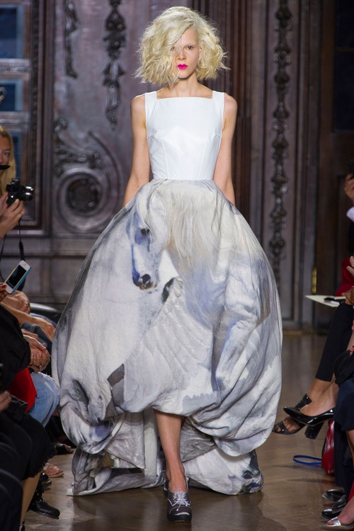 a blonde woman in a white and grey dress with a horse print. she is posing on the runway.