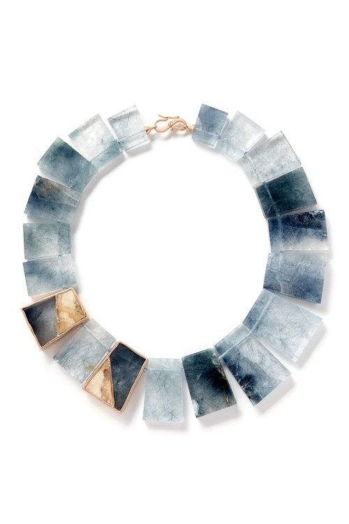 a closeup shot of a stunning aquamarine stone necklace, featuring a modern, geometric design. the stones are cut into rectangular shapes with a slight curve on one side, creating a beautiful, flowing pattern. the necklace is crafted from highquality materials, with a rose gold clasp that adds a touch of luxury. the aquamarine stones are various shades of blue, green, and gray, adding depth and richness to the piece. the necklace is perfect for dressing up any outfit and making a bold fashion statement.