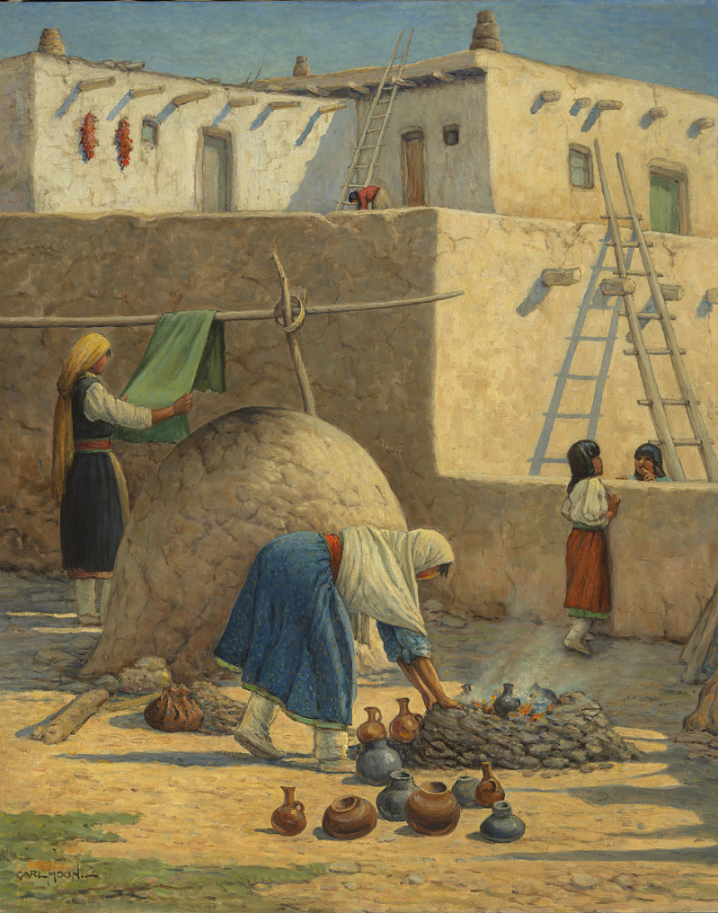 the painting is of a native american pueblo scene by carl moon. it depicts women and girls going about their daily lives. one woman is hanging a green cloth on a wooden structure, another woman is arranging pottery around a cooking fire, and two girls are looking over a wall. the scene is set in front of adobe buildings, with ladders leading to the roofs. red peppers are hanging on one of the walls.
