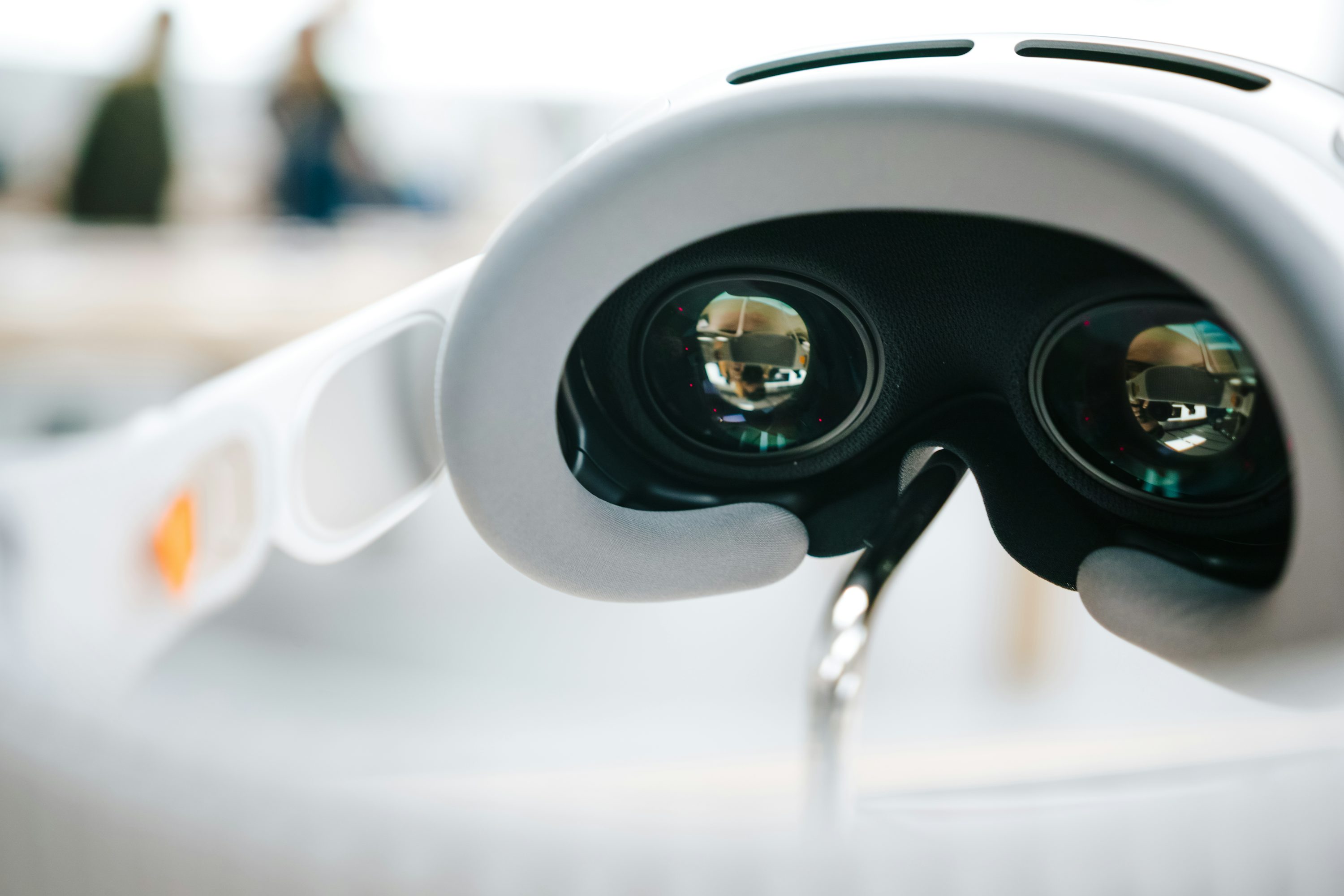 a closeup shot of a white vr headset, showcasing the lenses and overall design of the device. the lenses reflect the surrounding environment, indicating the immersive experience it provides.