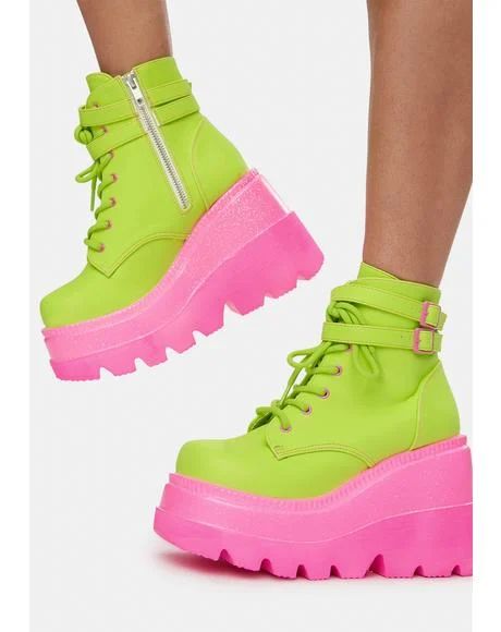 a photo of a pair of neon green platform boots with pink soles. the boots are lace up with a buckle around the ankle.