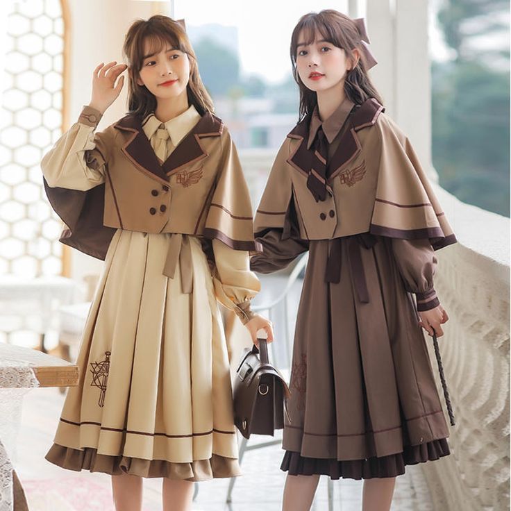 two asian women are posing for the camera. they are wearing lolita fashion outfits that have capes and matching purses. one woman is wearing a brown dress with a cream colored top and cape, and the other is wearing a cream dress with a brown top and cape.
