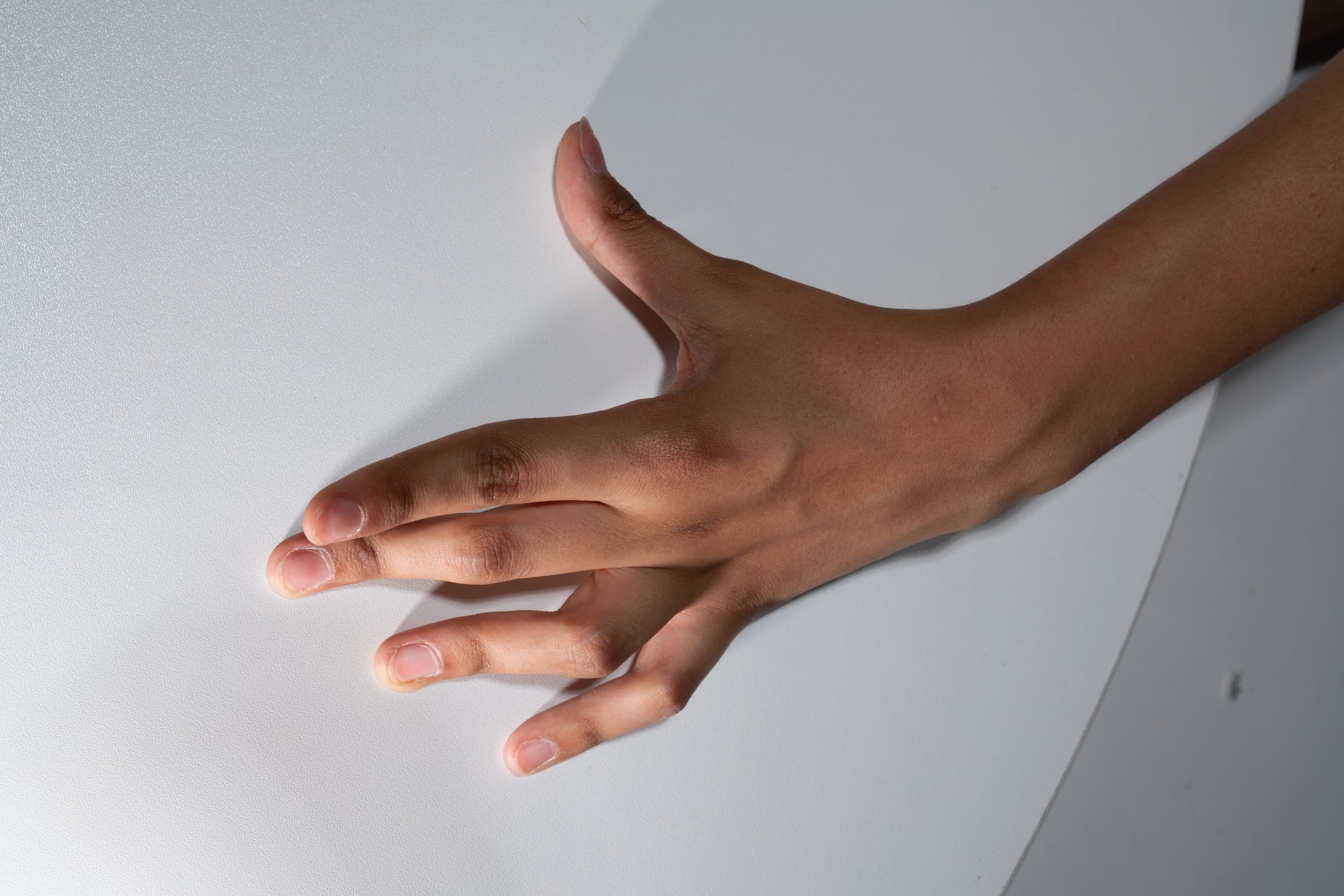 a closeup shot of a hand with brown skin gently touching a smooth, white surface with a subtle, glittery texture. the lighting is soft and natural, highlighting the details of the hand and the surface.