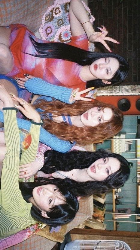 four women dressed in bright clothes pose for the camera on a couch in front of a vintage background.