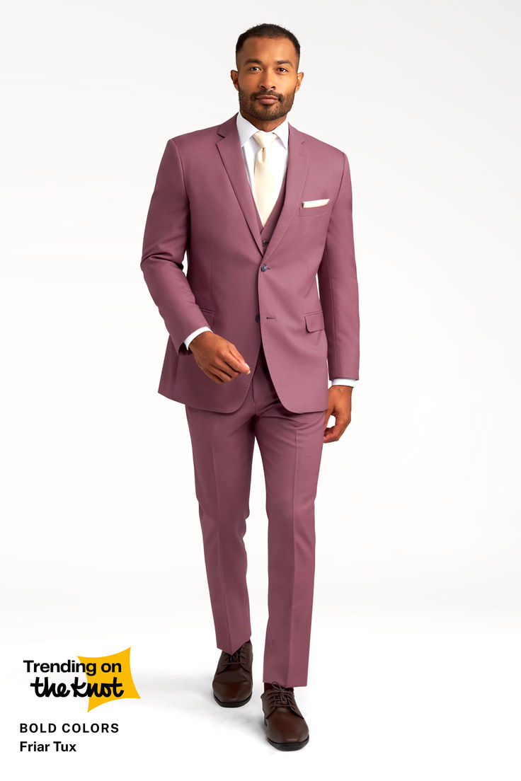 a fulllength studio shot of a man wearing a mauvecolored friar tux slimfit suit. he's wearing a light beige tie and brown dress shoes. the background is a plain light color.  a small graphic in the bottom left corner advertises "trending on the knot: bold colors friar tux".