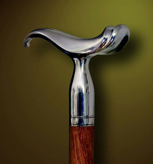 close up of a silver handle on a wooden walking stick. the handle is a very unique shape.  it looks like it may be handcrafted.  the wood is a dark brown.