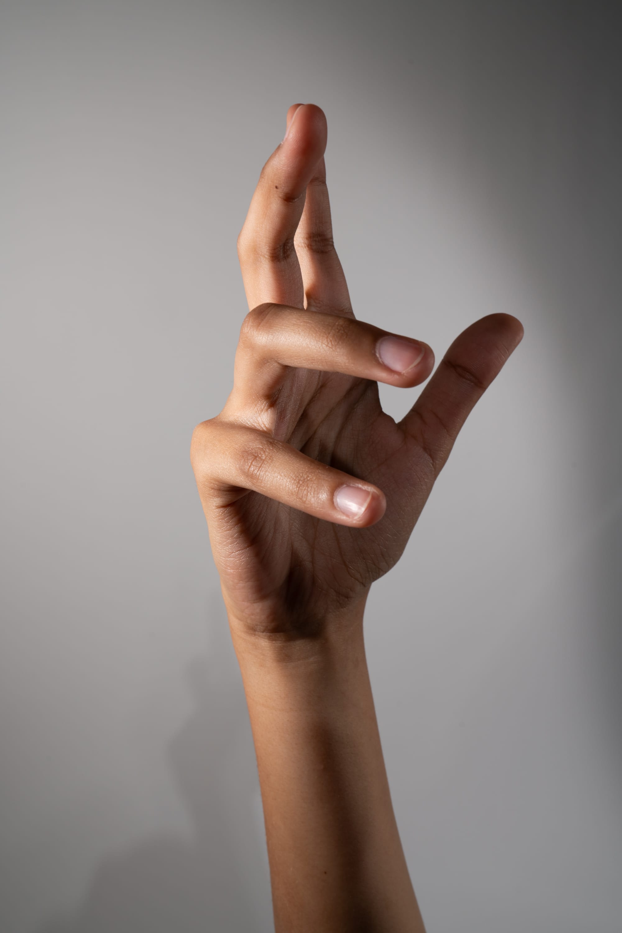 a closeup image of a hand with dark skin making a distinct gesture against a light gray background. the hand is lit with studio lighting, highlighting the details of the skin and fingers.