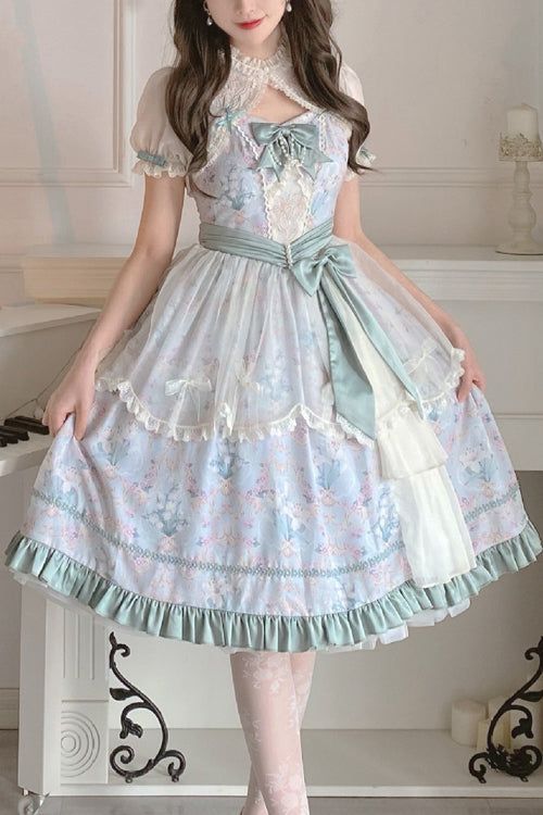 a woman is wearing a light blue and green lolita fashion dress. the dress has a floral pattern and is adorned with lace and tulle. she is standing indoors in a welllit room.