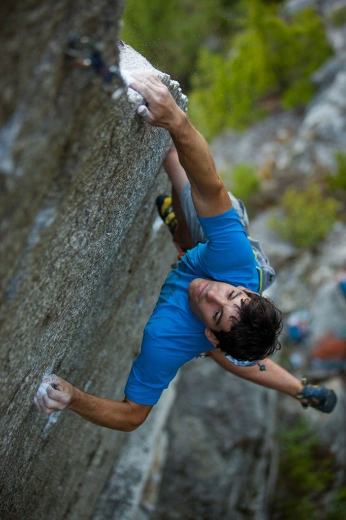 a rock climber hangs precariously from a steep rock wall, his body contorted into an impressive position. he looks focused and determined, his hands gripping the rock with precision and strength. the climber's blue shirt stands out against the gray rock wall, and his legs are almost completely obscured by the cliff.  the shot is taken from a low angle, giving a sense of the climber's vertical challenge. this image captures the essence of rock climbing: a combination of strength, agility, and mental focus, played out in a stunning natural setting.