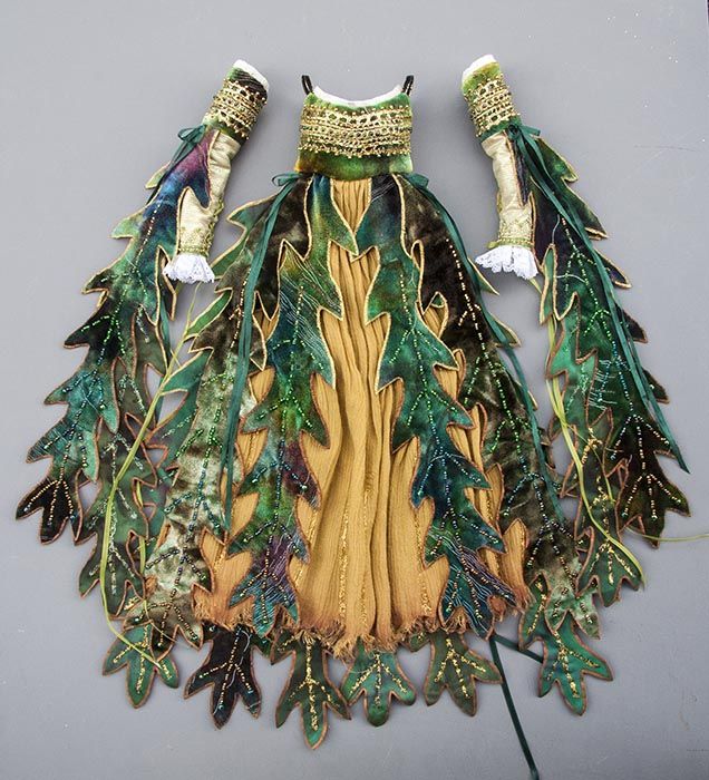 a fairylike costume, including a dress and sleeves, made of fabric and decorated with leaf patterns in green, brown, and gold. the dress has a yellow center panel with green leaf trim. the sleeves are gold with green leaf trim and white lace cuffs.