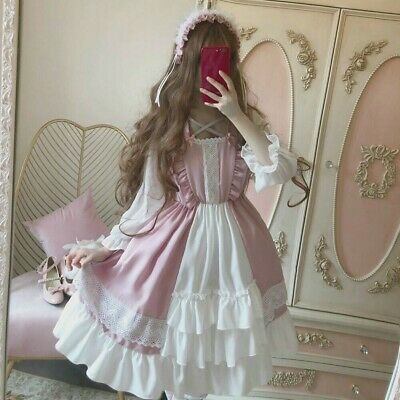 a young woman poses in a pink and white lolita fashion dress. the dress features delicate lace, ruffles, and a bow at the waist. she is also wearing a matching headband. the photo is taken in a room with a vintagestyle mirror and a pink chair.