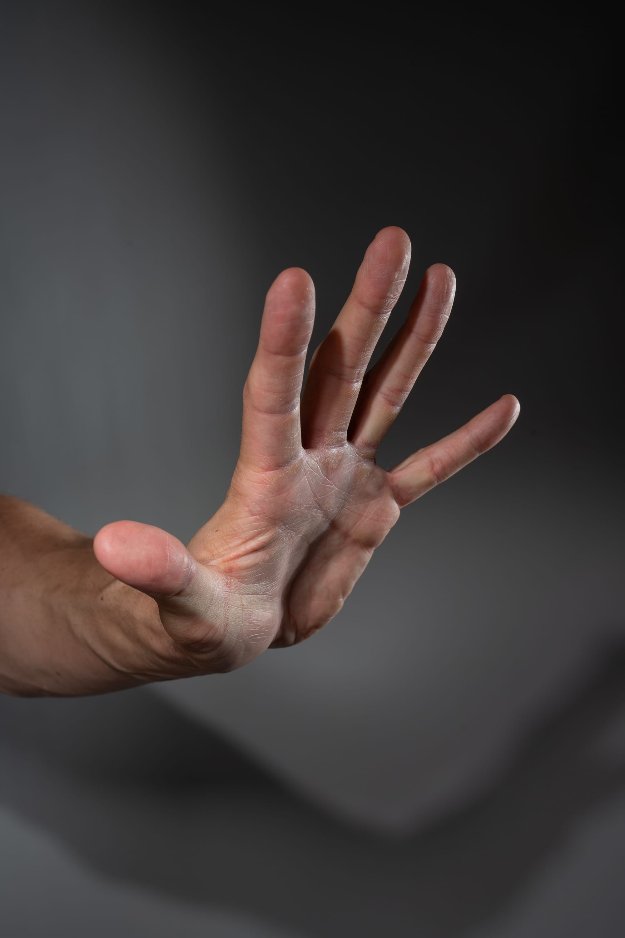 a man's hand is extended, palm out, in a gesture of stopping or halting. the background is a dark gray, and the hand is lit with studio lighting. the image is a closeup of the hand and arm.