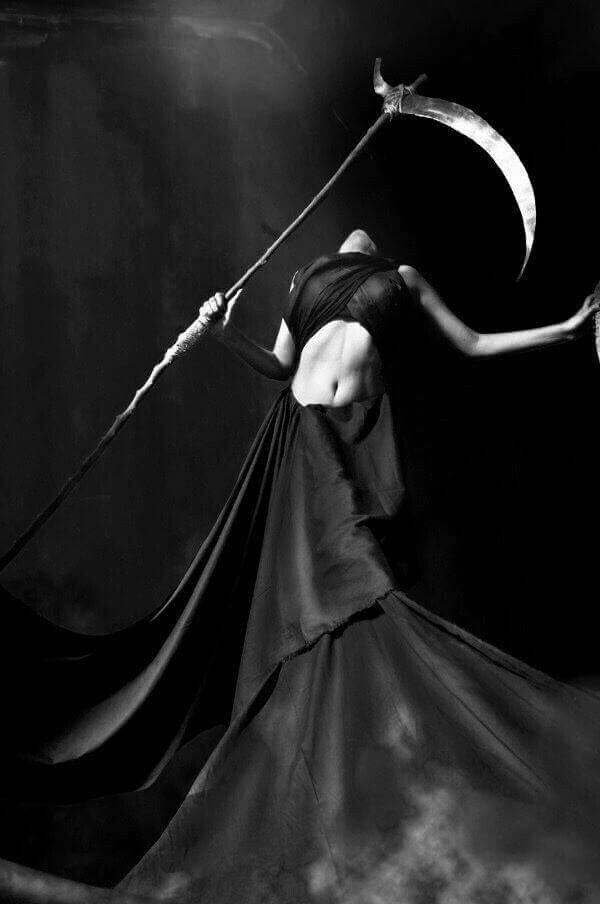 a woman in a flowing black dress holds a scythe in a dark, dramatic pose. the image is monochrome and full of shadows, creating a mysterious and gothic atmosphere.
