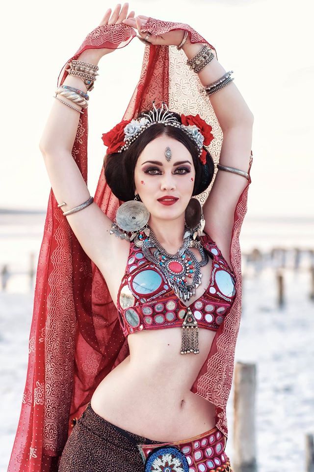 a beautiful belly dancer in a red sari with silver jewelry and a mirrorembellished bra poses in a desert setting. she is looking at the camera.