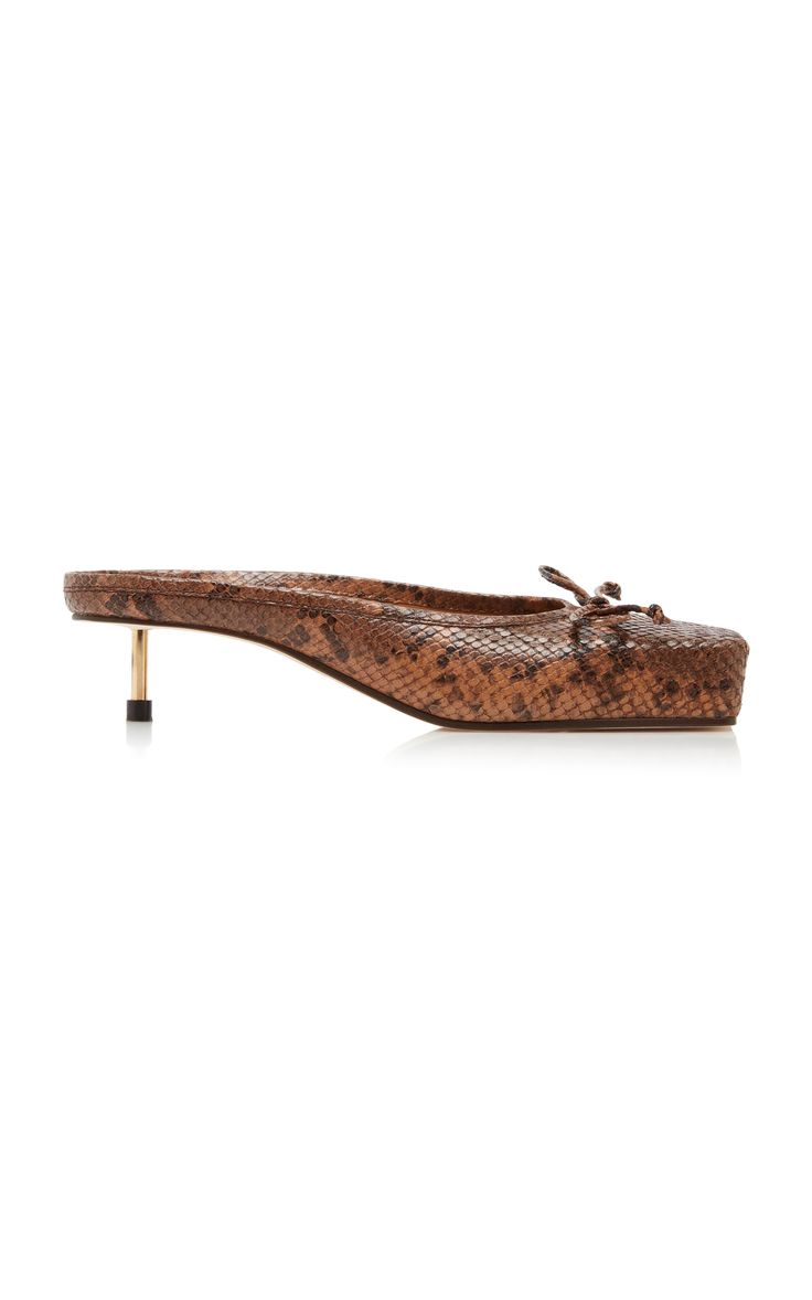 a pair of brown snakeskin mules with a low kitten heel and a square toe are shown against a white background. the mules have a small bow detail at the vamp.
