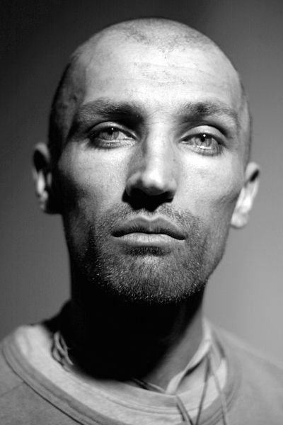 a black and white closeup portrait of a bald man with a beard, looking directly at the viewer with a serious expression.