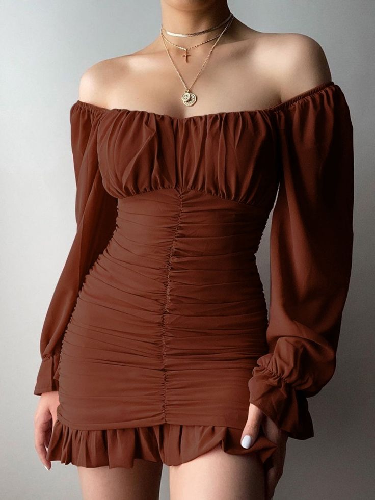 a woman is wearing a brown offtheshoulder long sleeve dress. the dress has a ruffle hem and is cinched at the waist. she is standing in a pose that shows off the dress.
