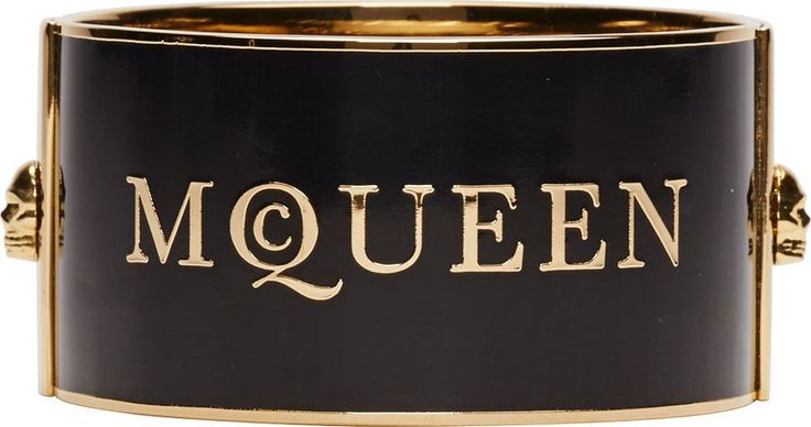 a black alexander mcqueen bracelet with gold trim and the brand name "mcqueen" in gold lettering across the front. there are skull details on the sides.