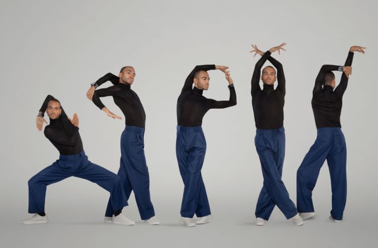 five male dancers in black shirts and blue pants are striking poses in a dance studio. they are all facing different directions and have different expressions on their faces, which creates a dynamic and interesting image. their movement and expression showcase their skill and talent as dancers.  the lighting and background of the image are simple, which allows the focus to be on the dancers and their poses.
