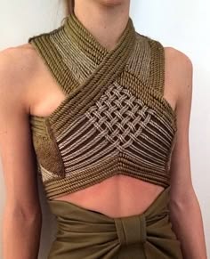 a closeup shot of a woman wearing a unique, handmade, ropebraided, brown crop top. she is posing with her arms at her side and the crop top is the center of the image. the top is intricately woven and crisscrosses at the front. the background is a simple, neutral color. the woman's skin is a nude color, which allows the top to stand out. this top is very stylish and unique and is perfect for a summer day.