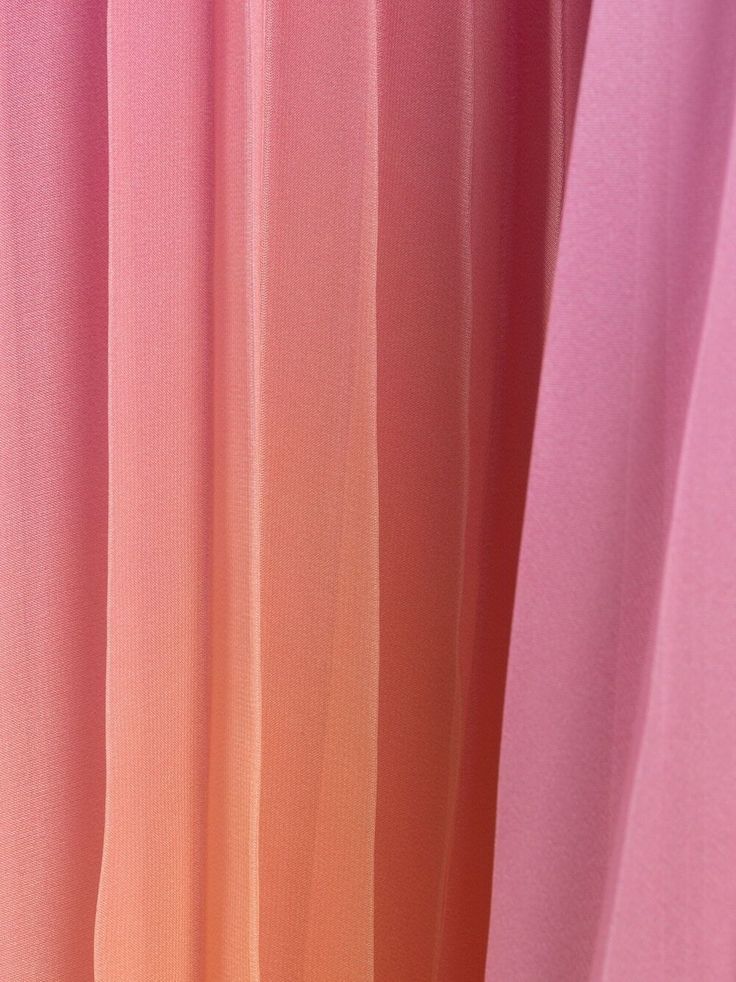 a closeup of pleated fabric with a gradient from pink to orange. the texture is visible, and the fabric drapes softly.