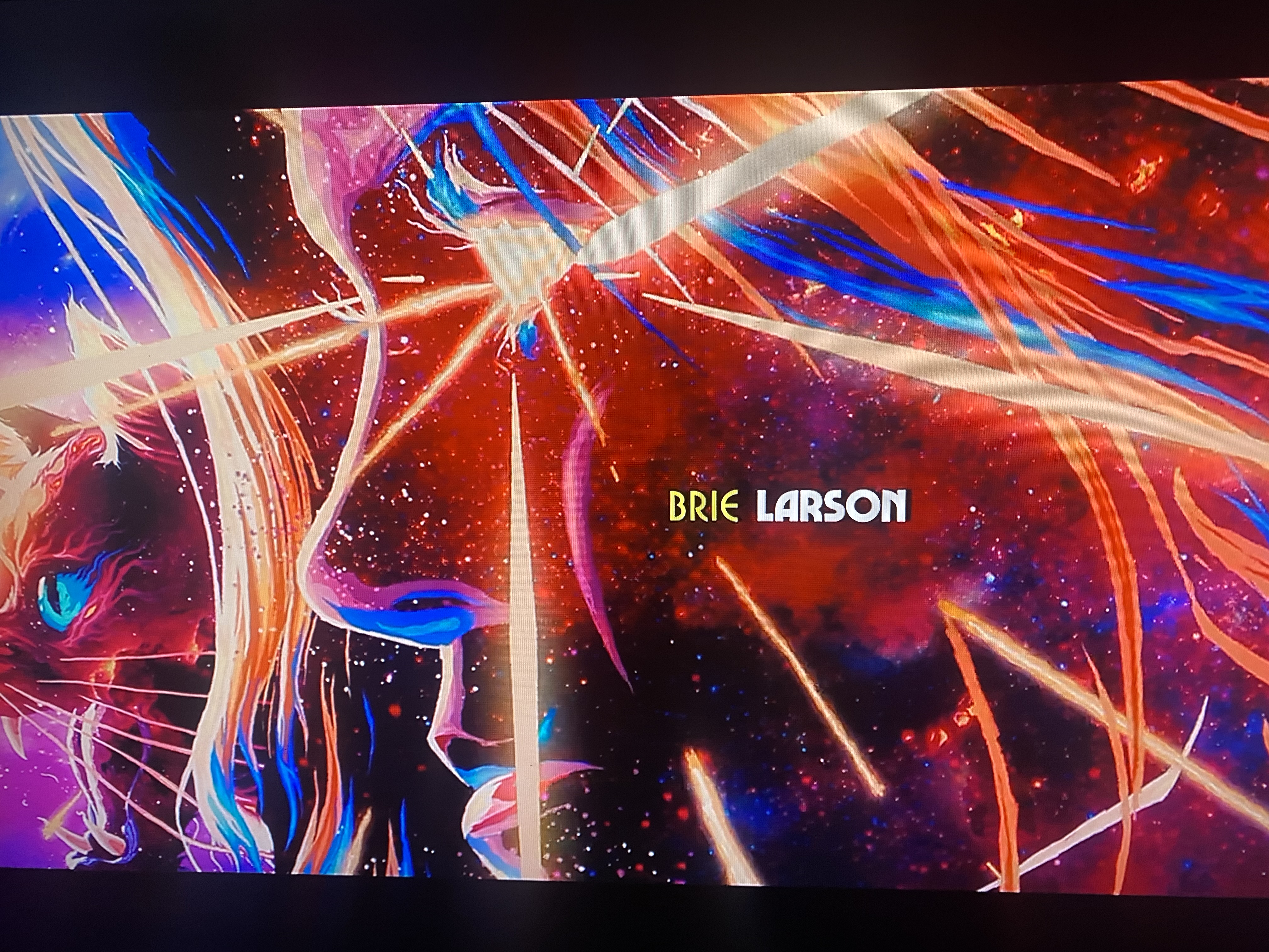 a digital illustration with  a  woman's face, a cat, and stars. the woman's face is lit up by a light source, and the stars are all around her. the words "brie larson" are displayed in yellow in the center of the screen. the image is colorful and has a fantasy futuristic look to it. it's likely from a movie or tv show.