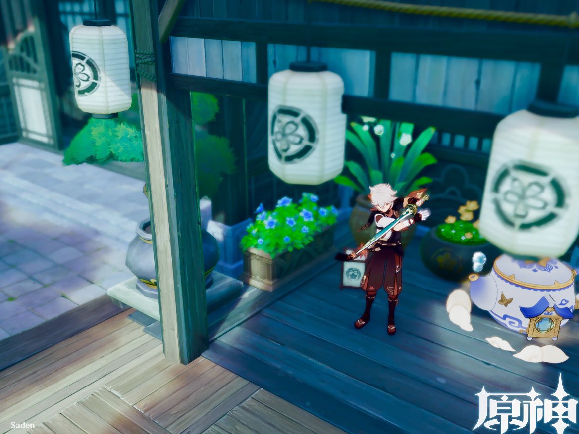 a screenshot from the video game genshin impact shows the character kaedehara kazuha standing outdoors in a japanesestyle setting, holding his sword.  he is positioned on a wooden deck or porch, surrounded by lanterns, plants, and flowers. a large teapot sits on the ground nearby. the architecture suggests a traditional japanese house or temple. the image is brightly lit and has an animeinspired aesthetic.  the game's logo is visible in the bottom right corner.