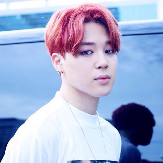 a portrait of park jimin of bts with pink hair, wearing earrings, makeup, a white tshirt, and a necklace.