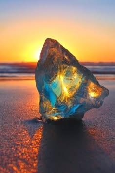 a closeup shot of a crystal clear rock, shaped like a mountain, resting on the beach. the rock reflects the colors of the sunset, creating a beautiful and vibrant scene. the rock is bathed in warm orange and yellow light, while the rest of the beach is bathed in a cooler blue light.