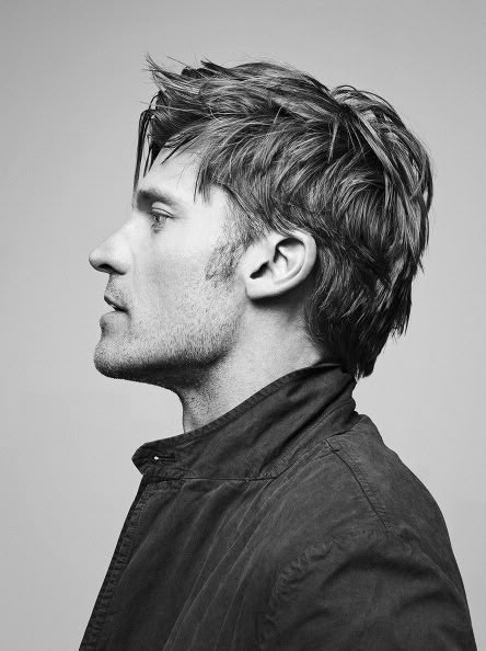 a black and white profile portrait of a handsome man with a stylish hairstyle, wearing a jacket. he has stubble and a defined jawline.
