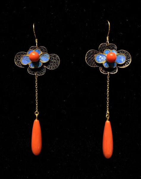 this is a closeup image of a pair of antique silver filigree earrings. each earring consists of a central blue cloisonné flower with a coral teardrop drop. the earrings dangle from delicate silver chains.
