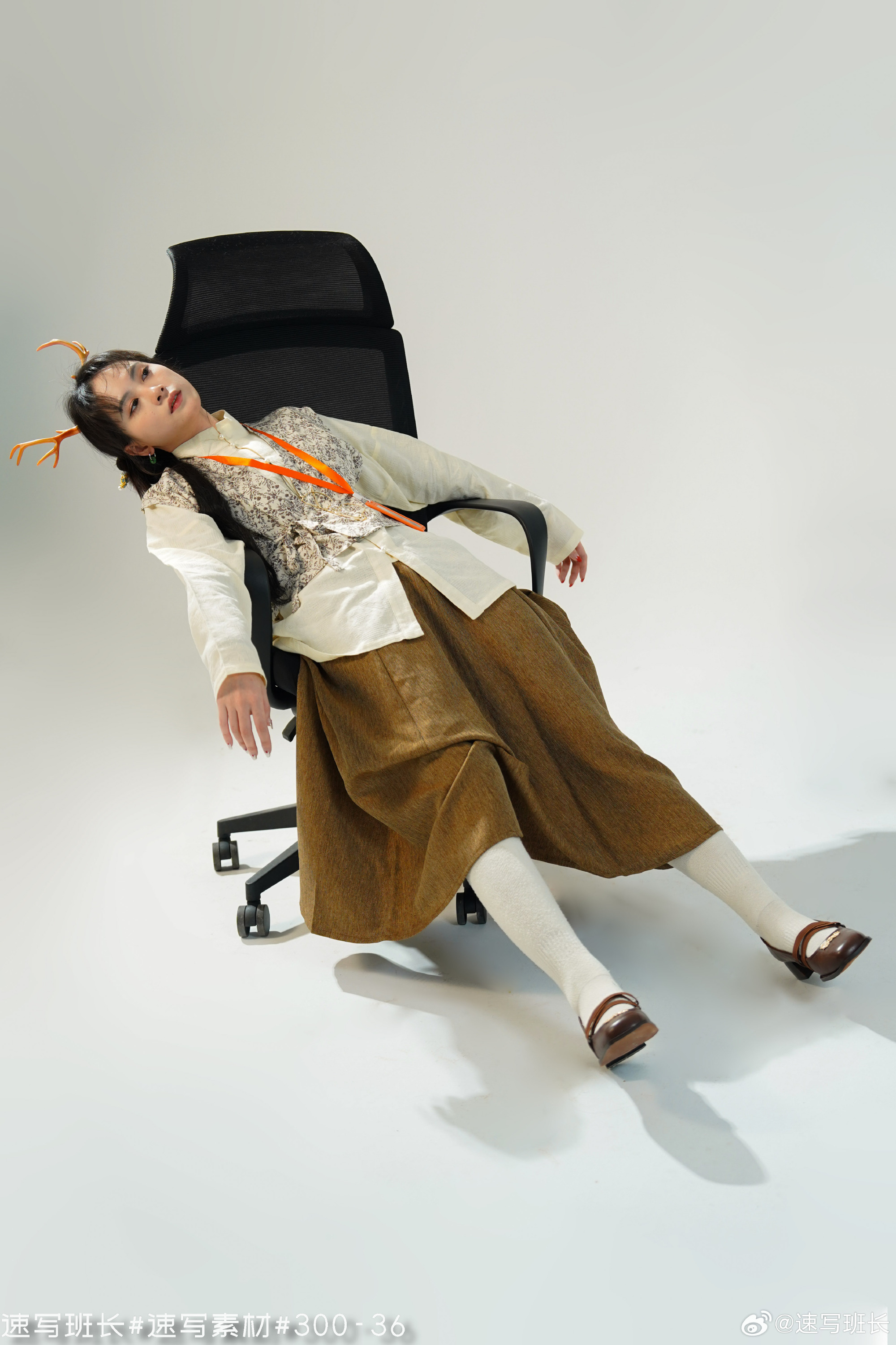 a young woman in a stylish outfit poses dramatically on an office chair in a studio setting. she wears a white shirt, a beige vest with embroidery, a brown skirt, white socks, and brown shoes. a headband with antlers adds a whimsical touch. the lighting is artificial, creating a clean and modern aesthetic. the image captures the model's unique style and personality.
