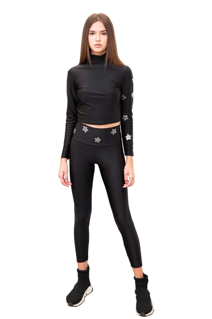 a fulllength shot of a young woman wearing a black starpatterned athletic outfit. the outfit consists of a longsleeved mock turtleneck top and highwaisted leggings. the model is standing against a white background and is wearing black sneakers. she has long brown hair and is looking directly at the camera. the image is professionally taken and showcases the clothing in a clear and concise manner.