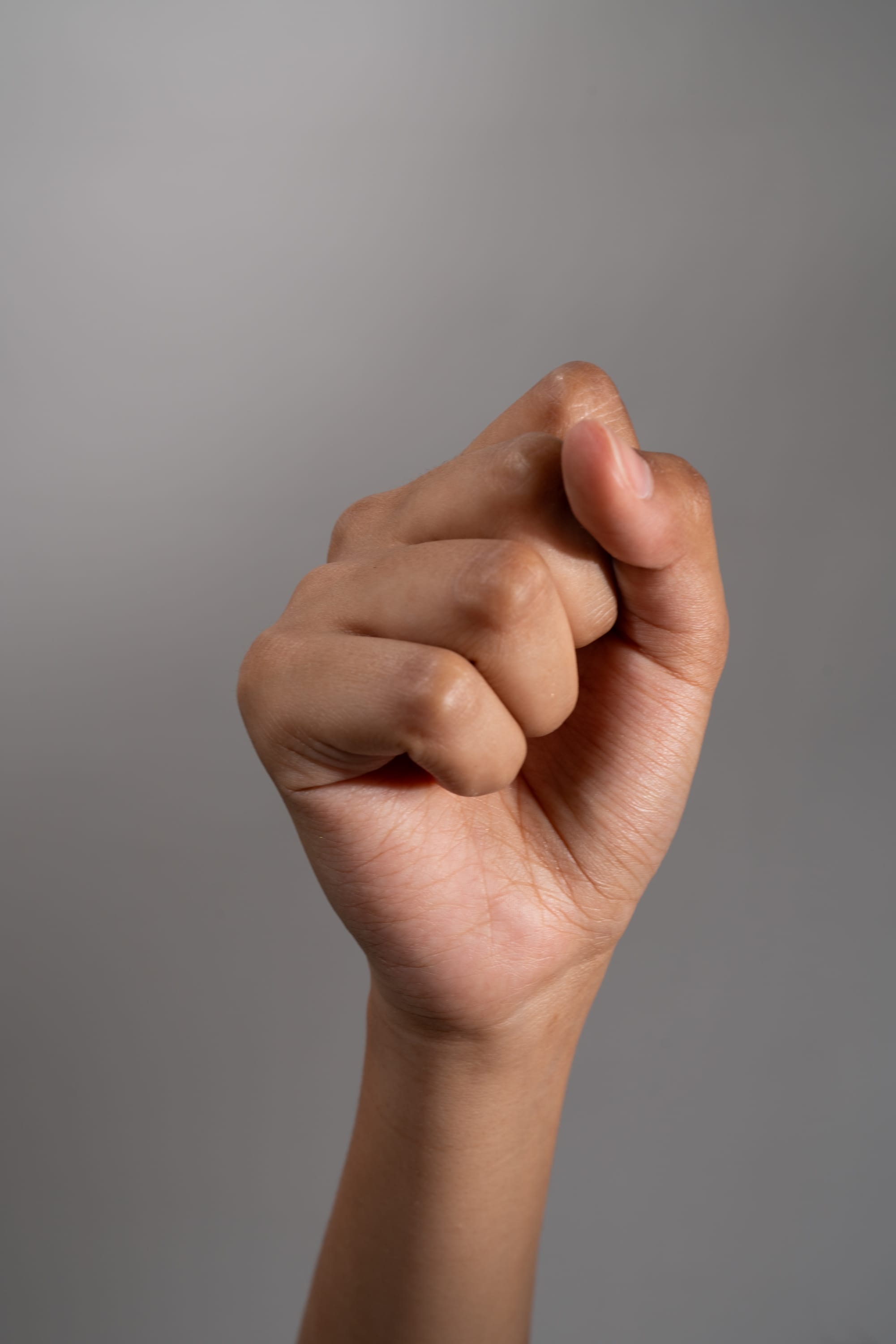 a person's hand is making a fist against a gray background. the hand is positioned in the center of the image with the fingers curled inward and the thumb resting on top. the image evokes feelings of strength, power, and solidarity. the lighting is soft and even, highlighting the details of the hand.