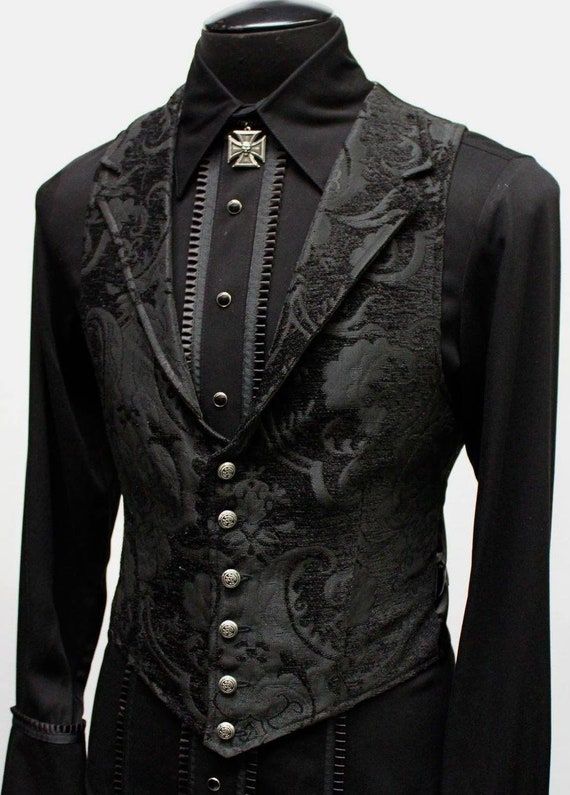 a black dress shirt and black vest on a mannequin. the vest has ornate designs and buttons. a metal pin is on the collar of the shirt.