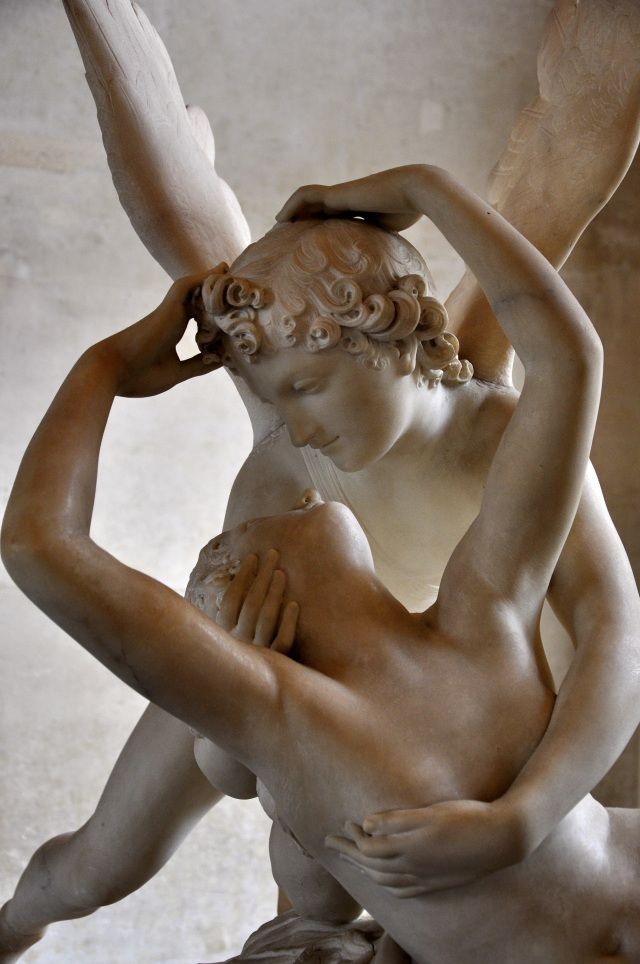the image shows a marble sculpture of cupid and psyche. cupid, with wings, is embracing psyche, who is gazing upwards. the sculpture is made of marble and shows the two characters as nude human figures. the piece represents the themes of love, mythology and art. the sculpture showcases the artistry of neoclassical art with emphasis on detail, with attention to the figures' bodies.