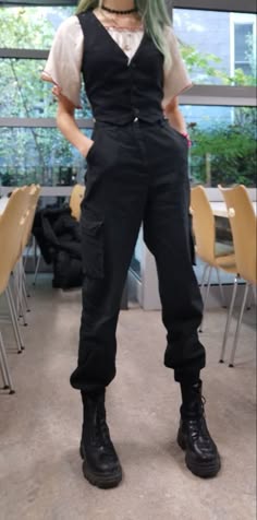 a young woman wearing a fashionable outfit of black pants, black vest, and a white shirt. she is standing in a casual setting and wearing black boots. the outfit gives off an edgy and trendy vibe.