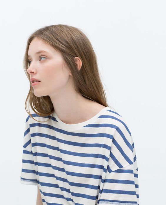 a young woman with long brown hair is wearing a blue and white striped tshirt. she is looking to her left, and her hair is falling over her right shoulder. the background is white, and the lighting is soft.