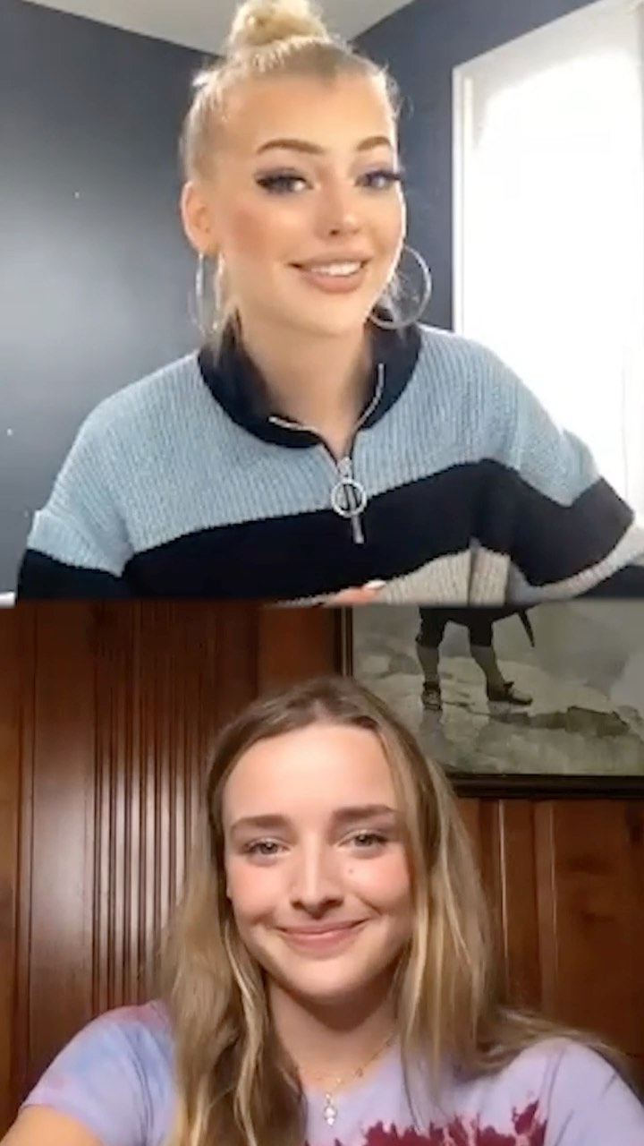 two women are on a video call. the woman on top has blonde hair in a bun, hoop earrings, and is wearing a blue and black sweatshirt. the woman on the bottom has long blonde hair and is wearing a tie dye shirt. the background behind the top woman is a blue wall and a white door. the background behind the bottom woman is wood paneling and a picture frame.
