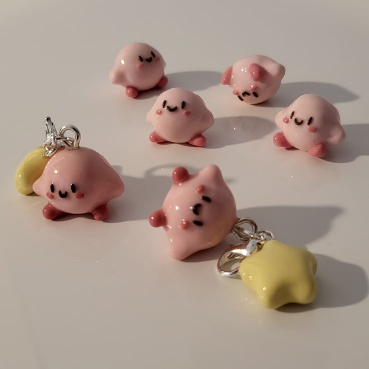the image shows six pink kirby charms, some with yellow star charms attached. they are handmade and appear to be made of clay. they are arranged on a white surface.