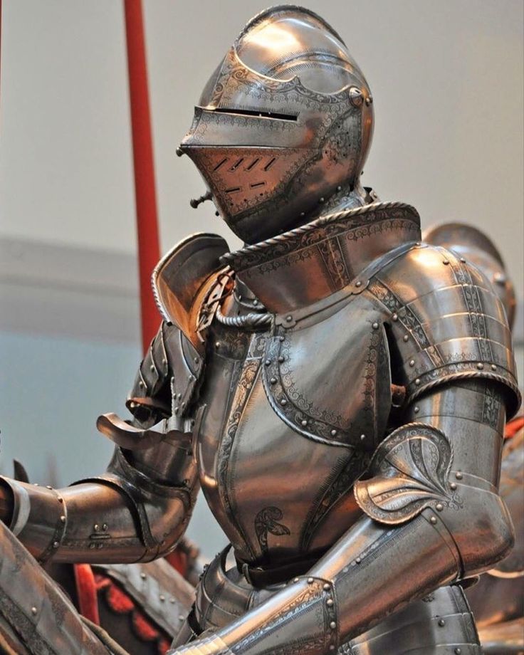 a closeup view of a suit of armor, a knight's suit of armor, is on display in a museum. the armor is made of steel and is intricately decorated. the helmet is closed, and the visor is down. the armor is in excellent condition, and the details are sharp and clear. the armor is mounted on a stand and is illuminated by spotlights. the background is out of focus. the suit of armor is a powerful and imposing piece of history, a reminder of the past and the dangers of war.