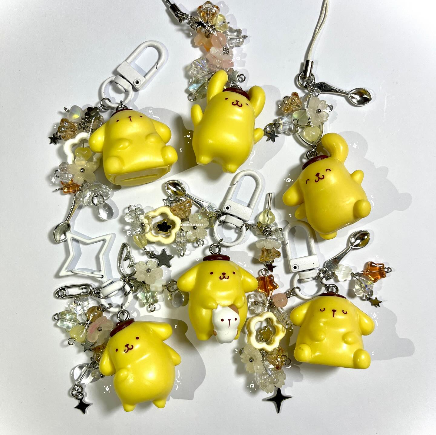 a collection of handmade pompompurin keychains and charms, featuring the popular sanrio character in various poses and outfits. the keychains are decorated with colorful beads, charms, and accessories, creating a cute and whimsical aesthetic.