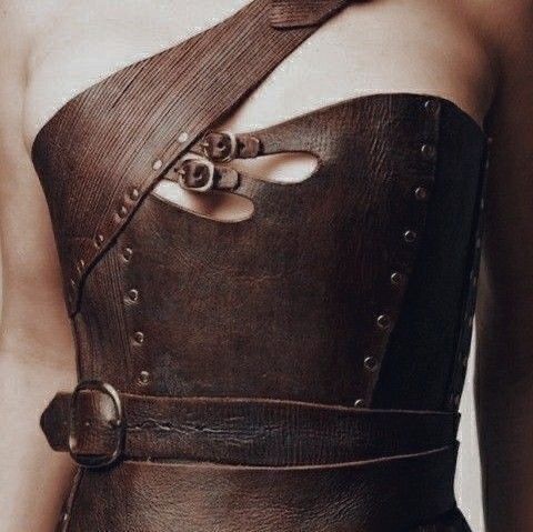 a woman is wearing a brown leather corset with straps and buckles. the corset is laced up the front and has a cutout design that reveals her skin. the corset is fitted and accentuates her figure. the woman is standing with her arms at her sides. the corset is made of highquality leather and is wellcrafted. the straps and buckles are sturdy and functional. the overall design of the corset is stylish and edgy. it is a unique piece of clothing that is perfect for a woman who wants to make a statement.