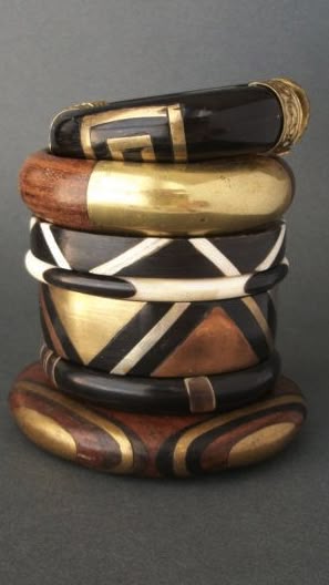 a stack of tribalstyle bracelets made of wood and metal. the bracelets have different patterns and designs, including geometric shapes and ethnic motifs. they are stacked on top of each other, creating a visually interesting display.