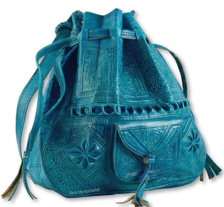 a blue leather drawstring bag with intricate embossed designs and a small pocket. it has tassels and is likely handmade in a moroccan style.