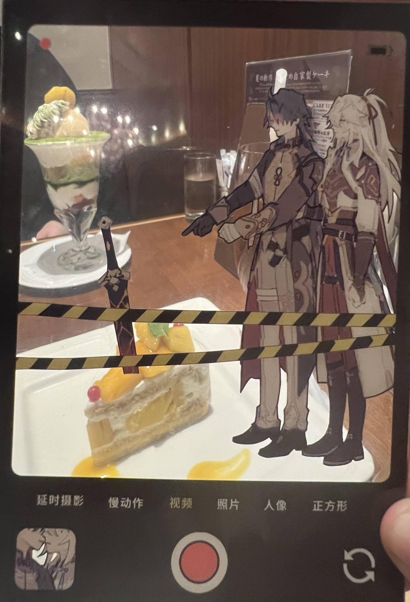 a photo on a smartphone screen of a delicious looking mango cake dessert, taken in a cafe.  there is a pair of anime characters from the game "genshin impact"  itto and albedo  standing on a table in the photo.  a second dessert is on the table, visible behind the cake.